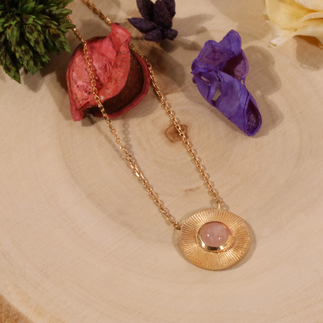 Le contraste entre le doré lumineux du plaqué or jaune et la teinte douce du quartz rose donne à ce collier une allure à la fois féminine, délicate et contemporaine. Son pendentif rayonnant attire subtilement la lumière et devient une véritable signature autour du cou.