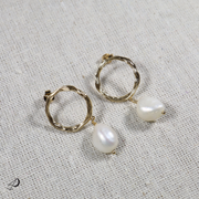 La boucle d'oreille de la collection Tautita est composée d'un pendentif rond doré avec une perle blanche couleur nacré.