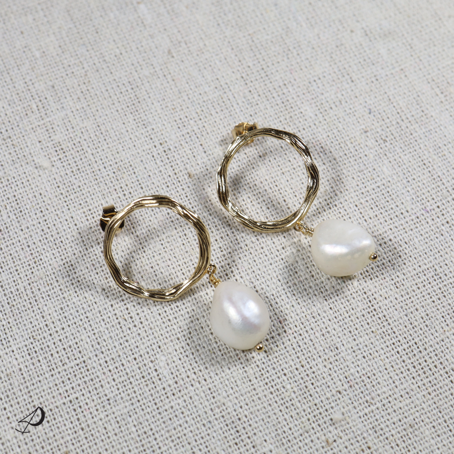 La boucle d'oreille de la collection Tautita est composée d'un pendentif rond doré avec une perle blanche couleur nacré.